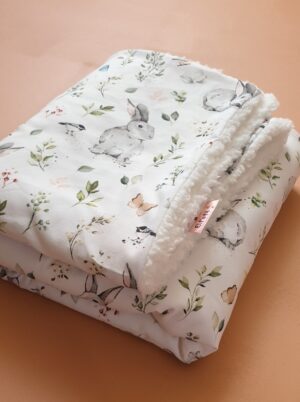 Couverture pour bébé, confectionnée avec un tissu coton à motifs lapins et doublée d'une douce fausse fourrure en sherpa blanche. Parfait pour offrir chaleur et confort à votre bébé.